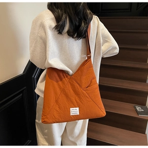 Detail view of large orange nylon crossbody bag featuring side pocket and quote label