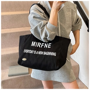 Detail of black canvas tote bag showing white slogan print and handmade metal logo tag
