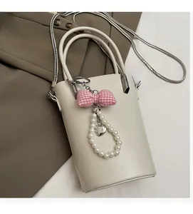 Detail einer beigen Beuteltasche mit rosa Karo-Schleife und Perlenherz-Anhänger auf Blazer
