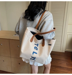 Détail du sac cabas en toile montrant les anses en cuir marron et le logo brodé