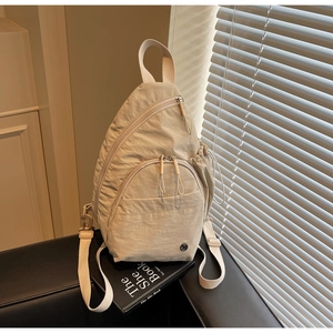 Detail of beige nylon backpack with multiple zipper pockets on a black leather sofa