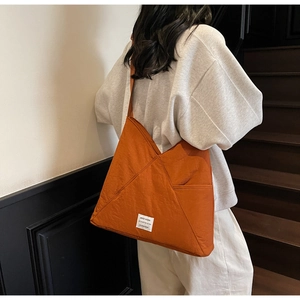 Detail of orange nylon shoulder bag featuring side pocket and square logo patch