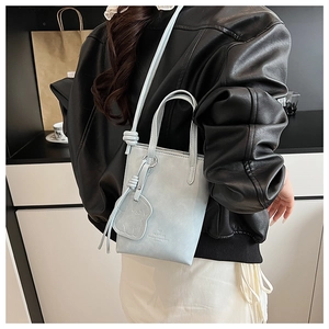 Detail of light blue mini tote bag featuring cute bear charm and embossed logo detail