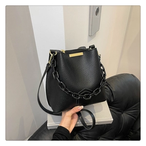 Détail d'un sac seau en cuir grainé noir avec une grosse chaîne mate et un ornement doré chic