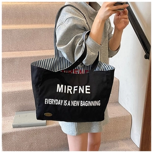 Detail of black canvas tote bag showing striped lining and white letter print