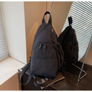 Close-up of black nylon chest bag with functional zipper layers and metallic logo detail