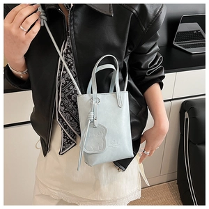 Close-up of light blue mini crossbody bucket bag with bear charm and embossed text