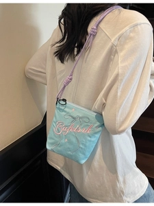 Light blue canvas crossbody bucket bag with purple braided strap and pink embroidery