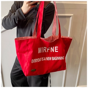 Detail of red canvas tote bag featuring white lettering and striped fabric handles