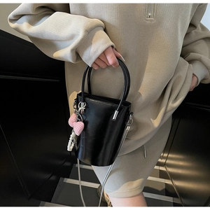 Detail der schwarzen Lack-Eimertasche mit Perlenanhänger und rosa Schleife am Gurt