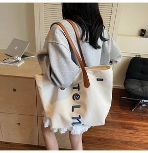 Détail d'un grand sac cabas en toile avec anses en cuir marron et broderie bleue