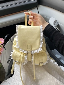 Pale yellow bucket backpack with white lace trim and decorative silver metal buckles