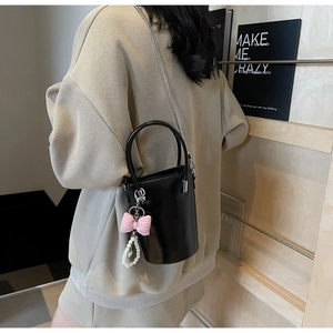 Detailansicht der schwarzen Lackleder-Eimertasche mit Perlenanhänger und rosa Schleife