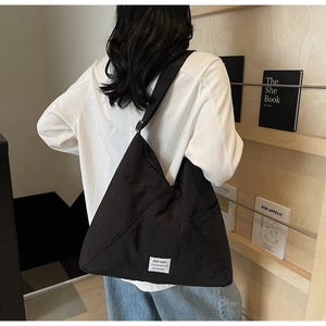 Detail of adjustable wide strap and white fabric label on black large nylon crossbody bag