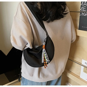 Detail of black crescent crossbody bag with personalized letter strap and orange cord pendant