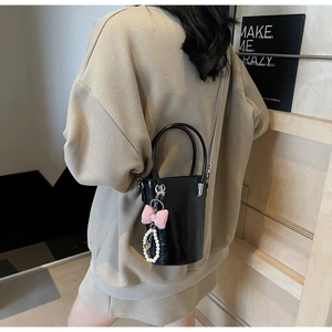 Detail der schwarzen Lackleder-Eimertasche mit rosa Schleife und Perlenherz-Anhänger