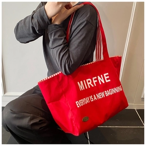 Detail of red canvas tote bag featuring white letter printing and red checkered strap lining