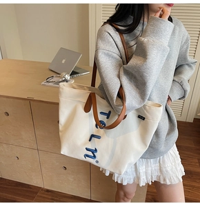 Détail d'un grand sac cabas en toile blanche avec anses en cuir marron et broderie TELN