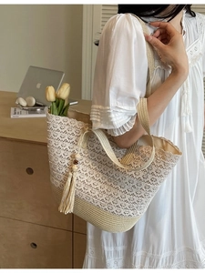Large beige woven straw tote bag with lace floral overlay and tassel on a female model