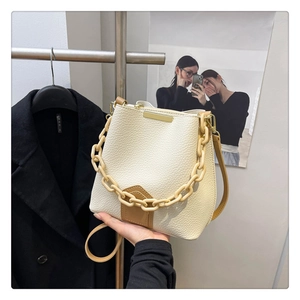 Détail du sac seau en cuir grainé avec chaîne en résine et finitions métalliques dorées