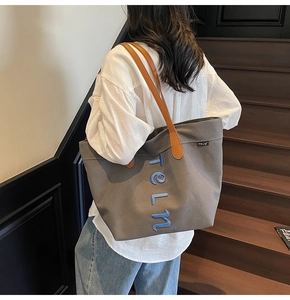 Détail du sac cabas en toile grise avec broderie bleue et anses en cuir marron
