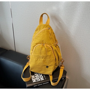 Detailed view of yellow nylon backpack with multiple zipper pockets on a black sofa