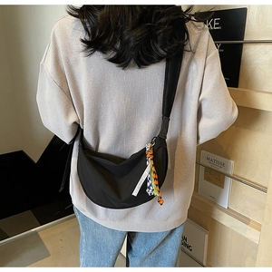 Detail of black nylon half-moon crossbody bag with colorful woven charms on shoulder strap