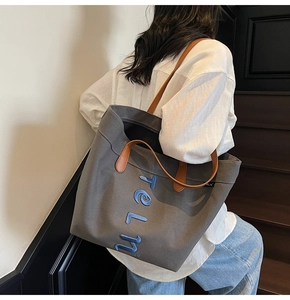 Détail du sac cabas en toile grise avec anses en cuir marron et lettrage brodé bleu