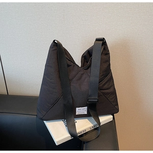 Detail of black quilted puffer tote bag showing white label and wide shoulder strap