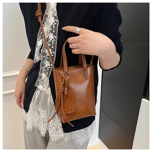 Close-up of brown leather mini bucket bag with a cute bear charm and adjustable strap