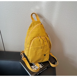 Detail of ginger yellow nylon sling bag showing multiple zippers and textile texture