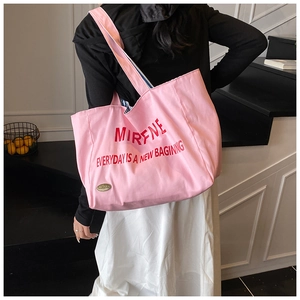 Detailed view of large pink canvas tote bag with red lettering on shoulder of female model