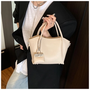 Detail of beige lychee grain leather handbag with a mini bag charm and silver chain