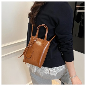 Brown mini bucket bag with leather handle, bear charm, and shoulder strap shown on model