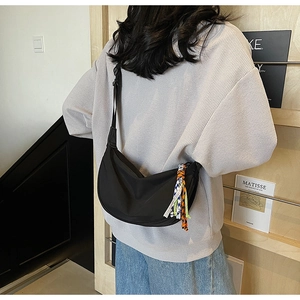 Detail of a black half-moon crossbody bag with a colorful woven tassel on a wide strap