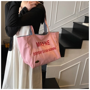 Pink canvas tote bag featuring blue striped handles and red slogan on indoor stairs