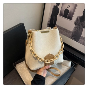 Gros plan du sac seau beige en cuir grainé avec chaîne en résine dans une boîte cadeau