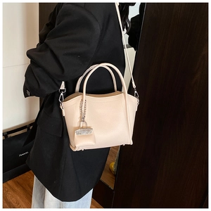Detail showing the lychee grain leather texture and mini bag charm on a beige handbag