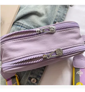 Detail of smooth silver zippers on a purple canvas crossbody camera bag with wide strap