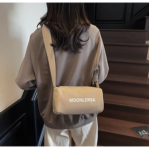 Detail view of the beige canvas cylinder bag showing wide shoulder strap and Moonlersa print