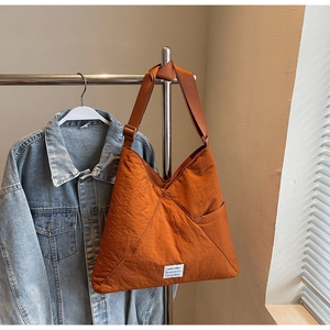 Detail view of burnt orange nylon shoulder bag featuring adjustable strap and woven logo tag