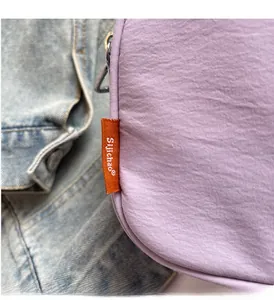 Detail of lavender canvas camera bag with orange logo tag on blue denim background