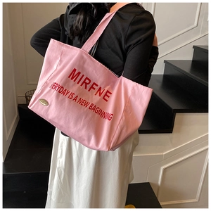 Rear view of model wearing a large pink canvas tote bag with bold red lettering