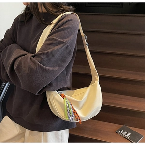 Detail showing cream crescent crossbody bag with colorful woven "NICENICE" charm