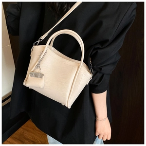 Detail of beige pebbled leather bucket bag with silver chain accessory and strap