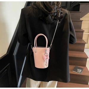 Rosa Eimertasche mit Perlenanhänger und Metallkette auf einer Holztreppe präsentiert