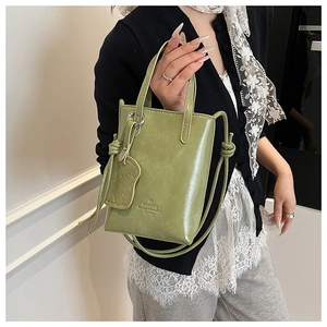 Close-up of a light green mini bucket bag with bear pendant and branded embossing
