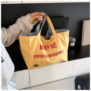 Detailed view of yellow canvas tote bag with red lettering and blue striped lining