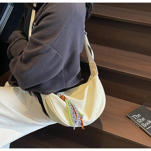 Beige half-moon crossbody bag with colorful NICE fringe keychain on a staircase