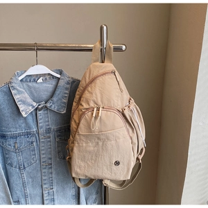 Detail of beige nylon crossbody chest bag with multi-pockets and metal logo on denim background